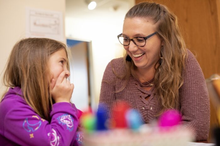 A smiling physiologist gets to know a second grade Groves Academy Learning Center student with a game.