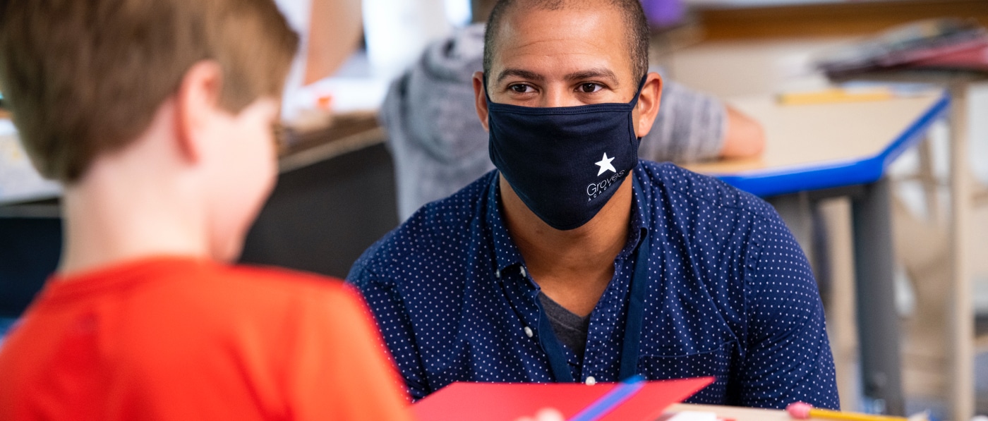 A masked Groves Academy Summer Programs educator works with a fourth-grade student.